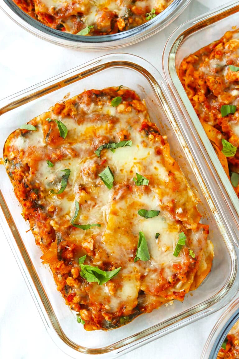 Red pesto chicken skillet lasagna in meal prep containers garnished with basil.