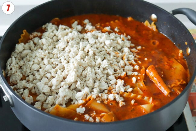 Cooked ground chicken added to pan with cooked lasagna noodles in red pesto tomato sauce.