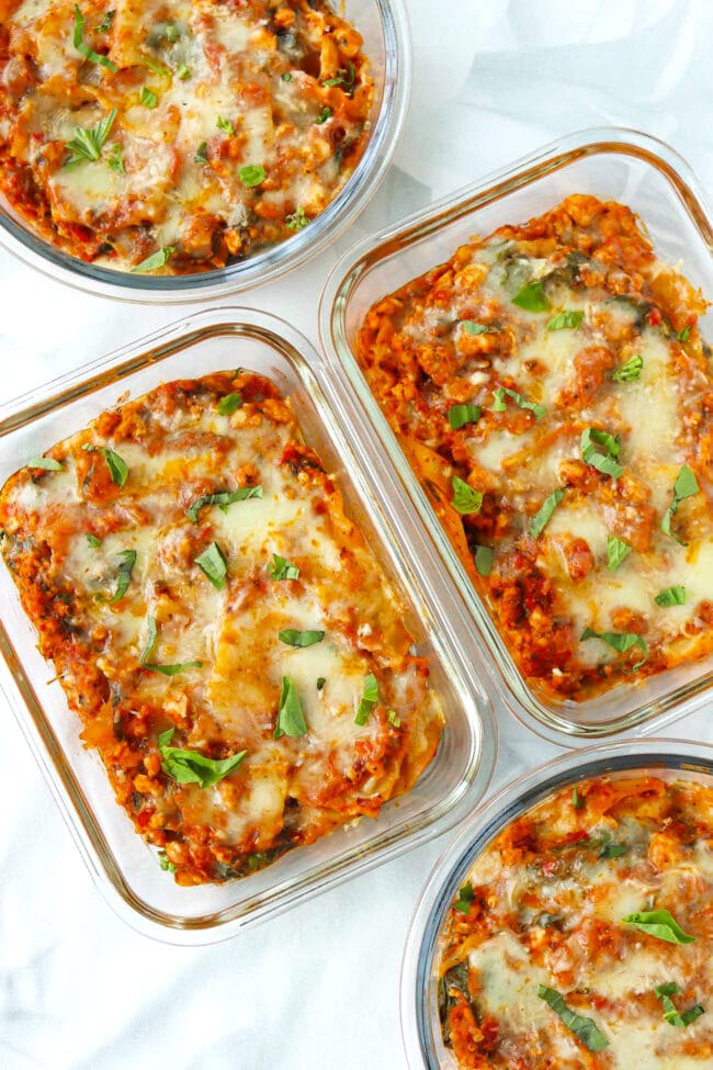 Red pesto lasagna in four glass dishes topped with sliced fresh basil.