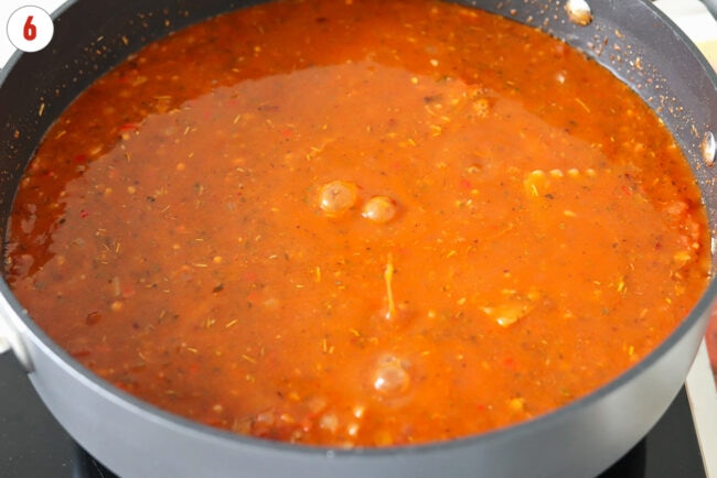 Red pesto tomato sauce with broken up lasagna noodles simmering in a pan.