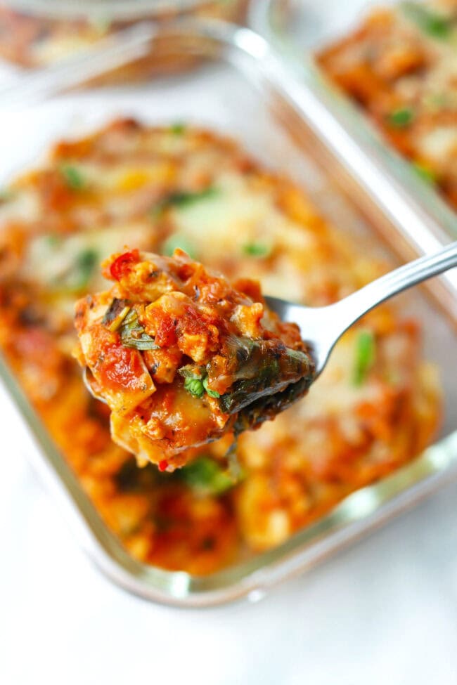 Closeup of spoon with a bite of red pesto lasagna.