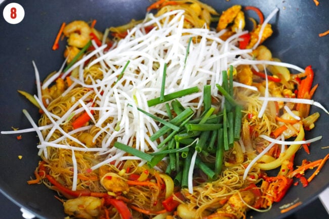 Mung bean sprouts spring onion in wok with Singapore noodles with chicken, shrimp, carrots, onion, and red bell pepper..