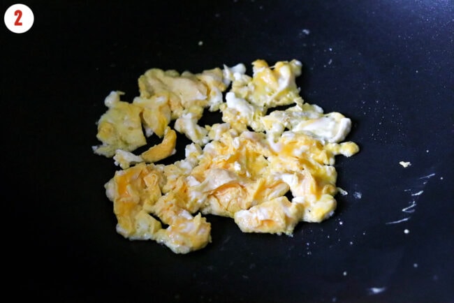 Half cooked scrambled egg in a wok.