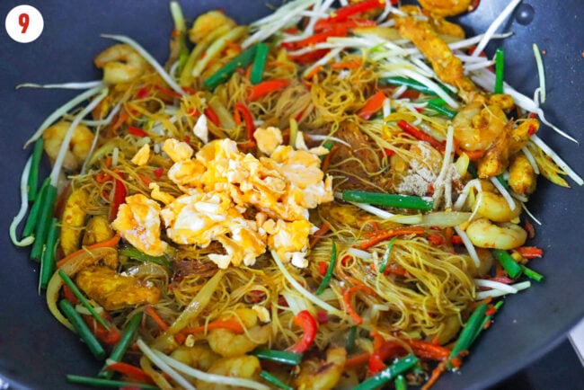 Scrambled egg in wok with Singapore Noodles with chicken, shrimp and vegetables.