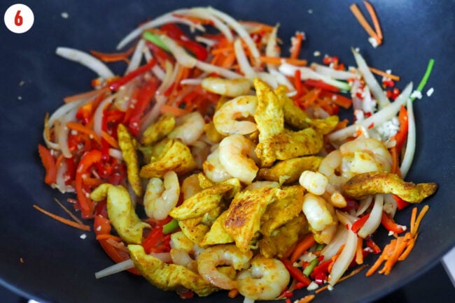 Cooked shrimp and curry powder seasoned chicken pieces in a wok with stir-fried vegetables.
