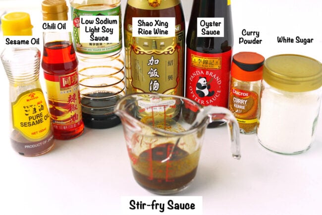 Labeled sauce ingredients for Singapore Noodles on a white background and sauce in a measuring glass.