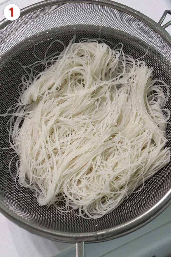Rehydrated thin rice vermicelli noodles in a fine mesh strainer.