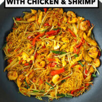 Stir-fried curry noodles with chicken, shrimp, egg and vegetables in a wok. Text overlay "Singapore Noodles with Chicken & Shrimp" and "That Spicy Chick".