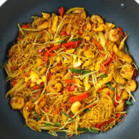 Wok with stir-fried Singapore curry noodles with chicken, shrimp, egg and vegetables.