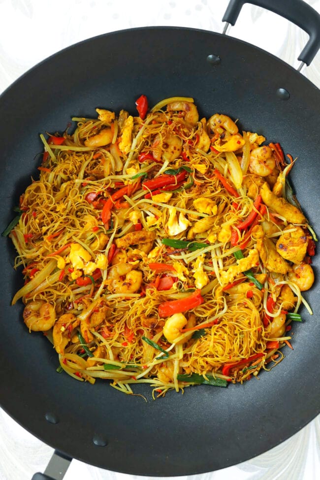 Wok with stir-fried Singapore curry noodles with chicken, shrimp, egg and vegetables.