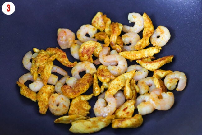 Cooked curry powder seasoned chicken and shrimp in a wok.
