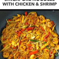Wok with yellow curry thin rice noodles with chicken, shrimp and vegetables. Text overlay "Higher Protein", "Singapore Noodles with Chicken & Shrimp" and "That Spicy Chick".
