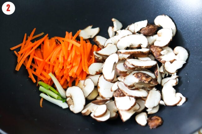 Sliced carrots, mushrooms and spring onion white and light green parts in a wok.