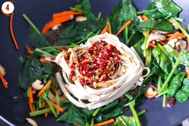 Tofu noodles and sauce with chopped red chilies and garlic added to wok with stir-fried spinach, carrots, and mushrooms.
