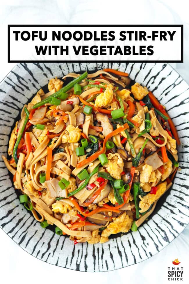 Plate with stir-fried noodles made from tofu with spinach, mushrooms, carrots, eggs, and turkey. Text overlay "Tofu Noodles Stir-fry with Vegetables" and "That Spicy Chick".