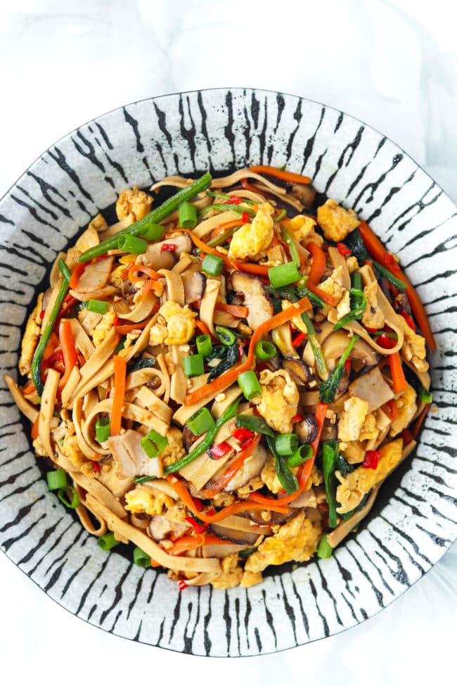 Closeup of plate with stir-fried noodles made from tofu with spinach, mushrooms, carrots, eggs, and turkey.