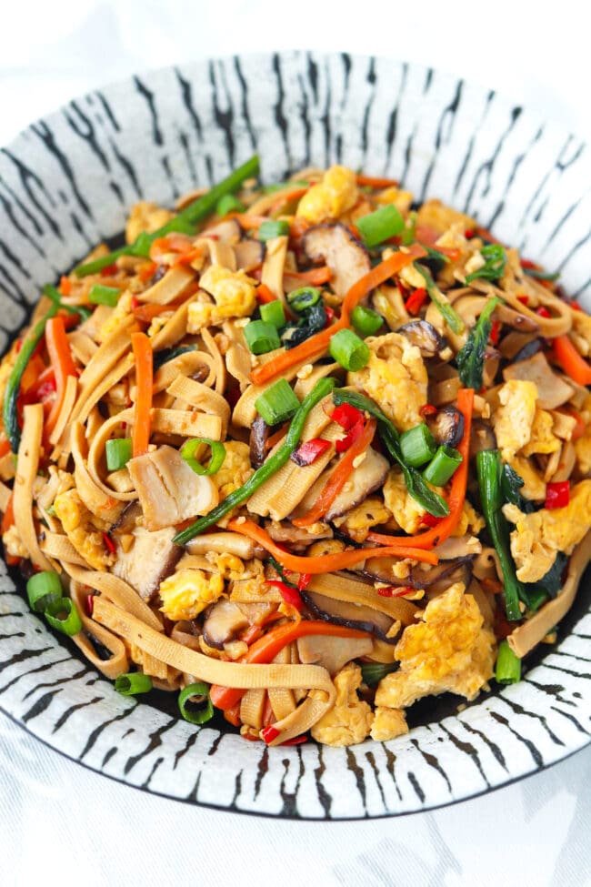 Front view of plate with tofu noodles stir-fry with spinach, mushrooms, carrots, eggs, and turkey.