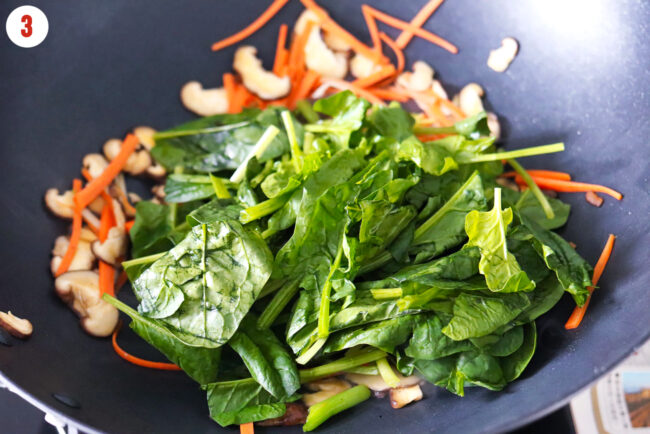 Chinese spinach in wok with stir-fried carrots and mushrooms.