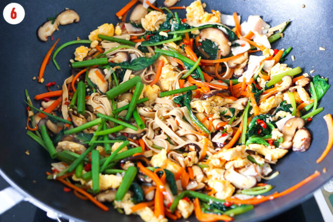 Green onions added to tofu noodles stir-fry with vegetables in a wok.