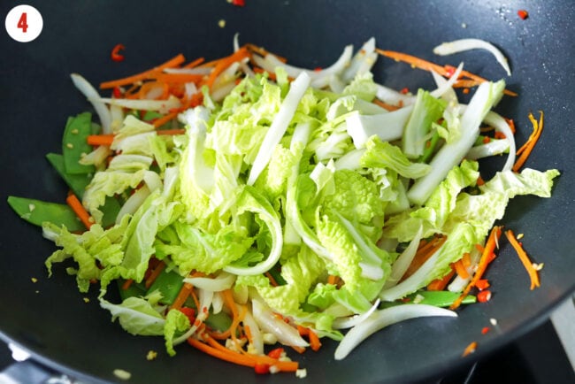 Sliced Chinese cabbage in wok with stir-fried onion, snow peas, carrots, garlic and red chilies.