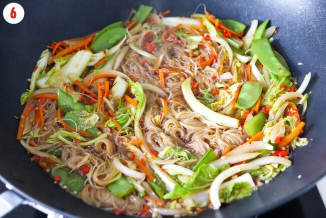 Rice vermicelli noodles simmering in a wok with vegetables and a broth and soy sauce mixture.