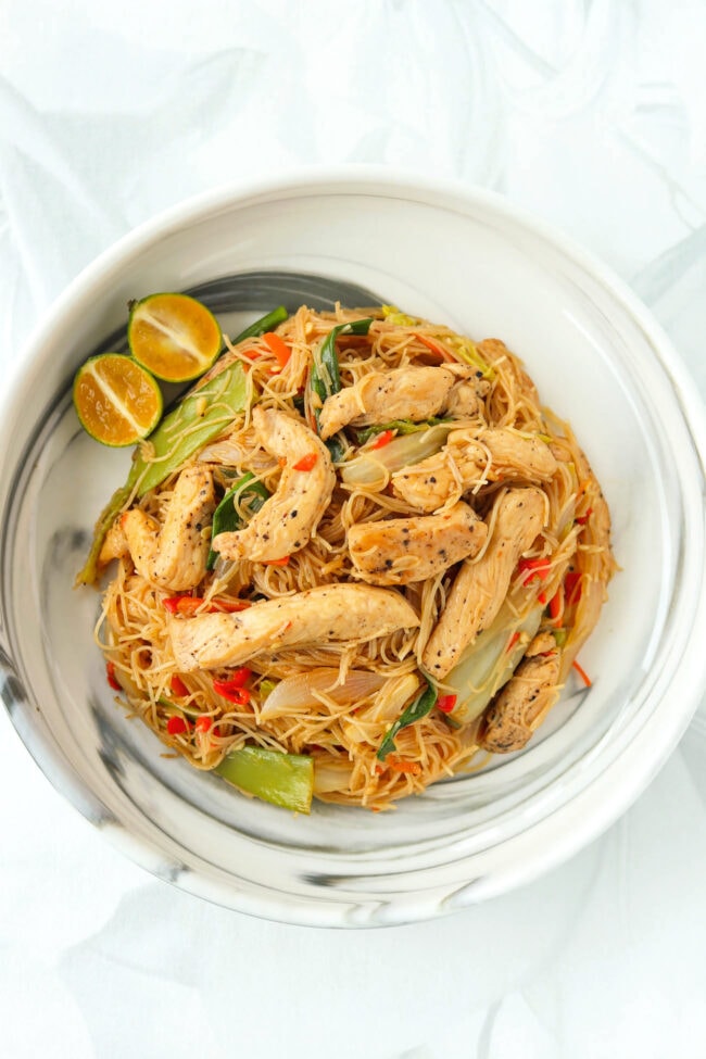 Top view of plate with pancit bihon with chicken and calamansi wedges.