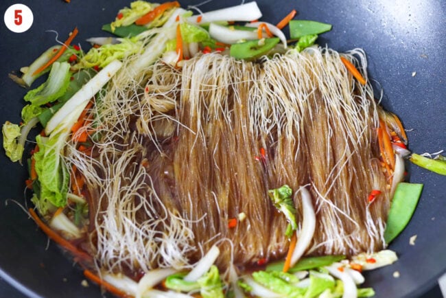 Thin dried rice vermicelli noodles, broth and soy sauce mixture in wok with stir-fried vegetables.