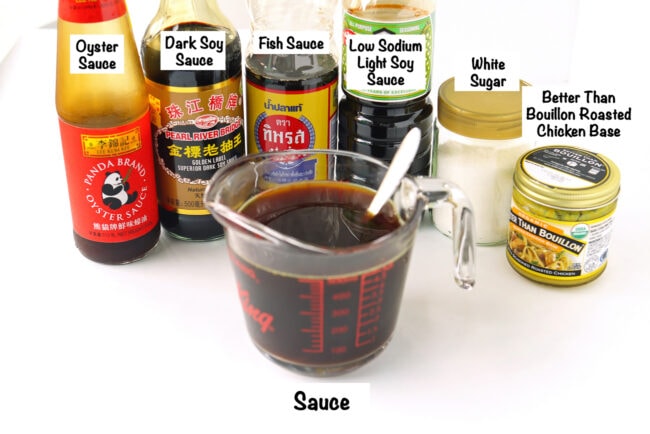 Labeled sauce ingredients bottles and a soy sauce and broth mixture in a large measuring glass with a spoon.