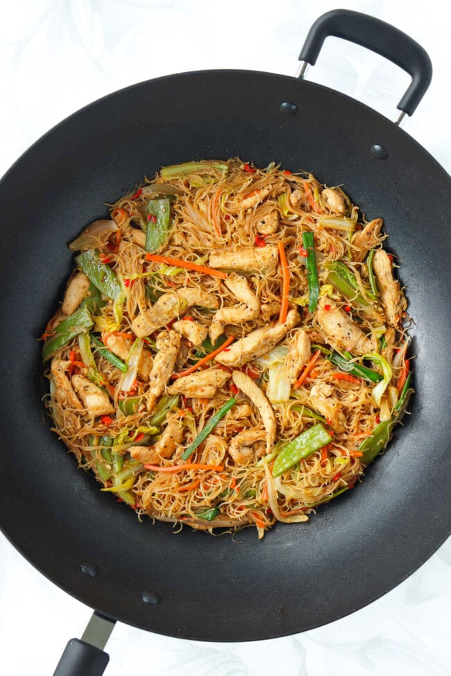 Pancit bihon noodles with chicken and vegetables in wok.