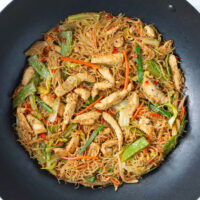 Closeup of pancit bihon noodles with chicken and vegetables in wok.