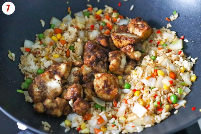 Air fryer tofu pieces on fried rice with vegetables in a wok.