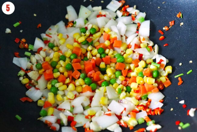 FRozen mixed vegetables, yellow onion, garlic and red chilies in a wok.