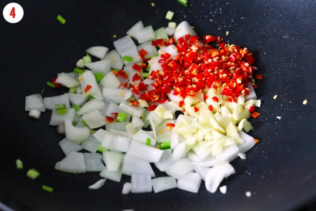 Diced yellow onion, garlic, fresh red chilies and light green onions in a wok.