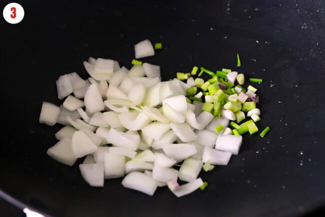 Yellow onion and spring onion white and light green parts in a wok with peanut oil.