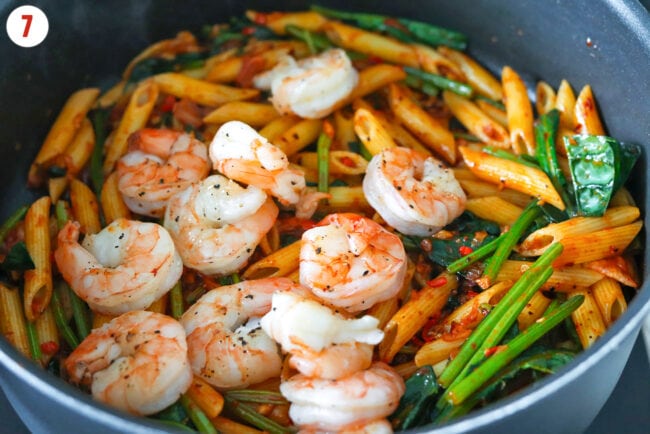 Cooked shrimp, wilted spinach and spicy kimchi pasta in a skillet.
