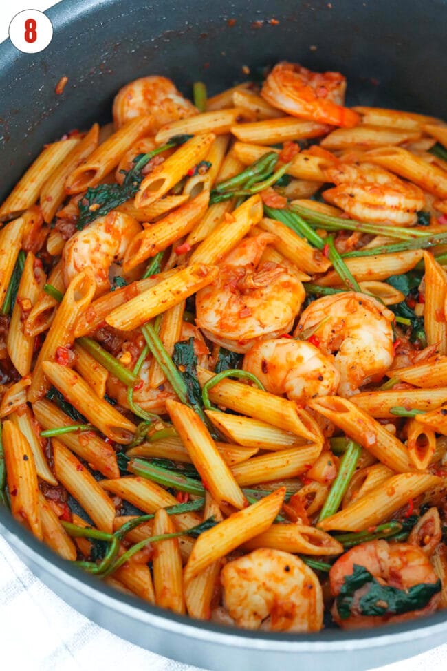 Closeup of spicy kimchi pasta with spinach and shrimp in a pan.