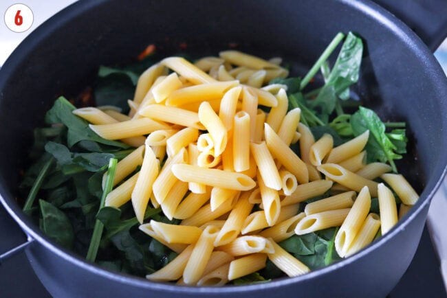 Cooked penne pasta and spinach in a skillet.