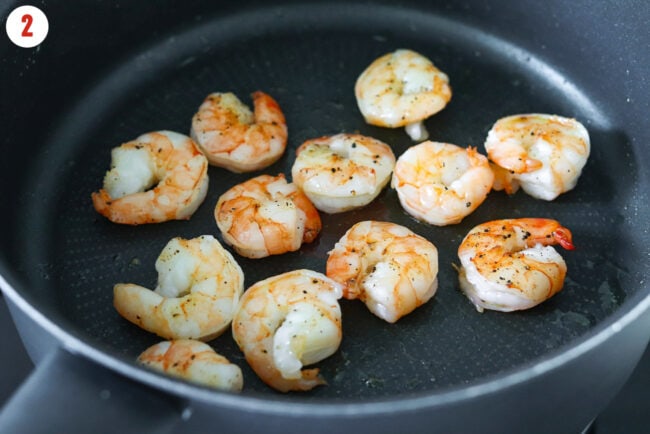 Cooked salt and pepper seasoned jumbo shrimp in a skillet.