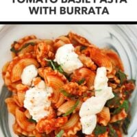 Plate with tomato basil pasta and spinach topped with basil and black pepper seasoned torn burrata. Text overlay "Easy Weeknight Dinner!", "Tomato Basil Pasta with Burrata" and "That Spicy Chick".