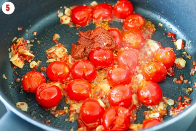 Harissa and burst cherry tomatoes in a skillet with sautéed garlic, chilies and shallots.