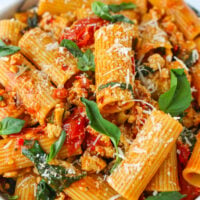 Closeup front view of plate with harissa pasta with cherry tomatoes, spinach, and basil topped with grated parmesan cheese.