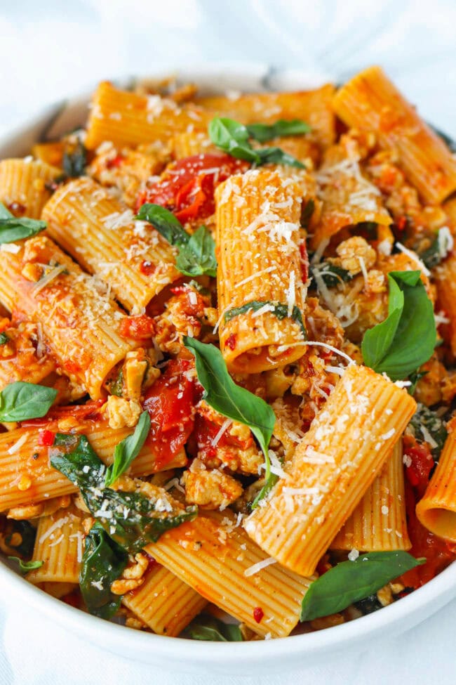Closeup front view of plate with harissa pasta with cherry tomatoes, spinach, and basil topped with grated parmesan cheese.