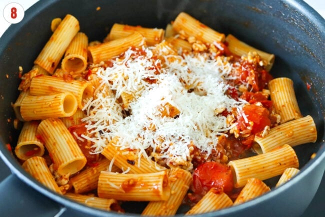 Freshly grated Parmigiano Reggiano cheese in a pan with harissa and burst cherry tomato pasta with chicken.