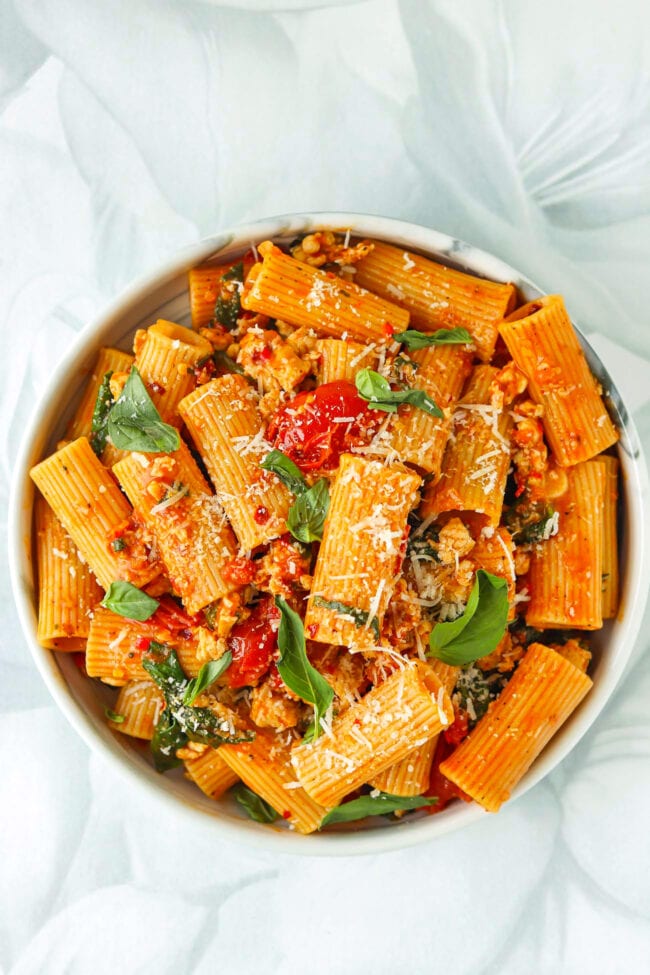 Top view of plate with harissa pasta with cherry tomatoes, spinach, and basil topped with grated parmesan cheese.