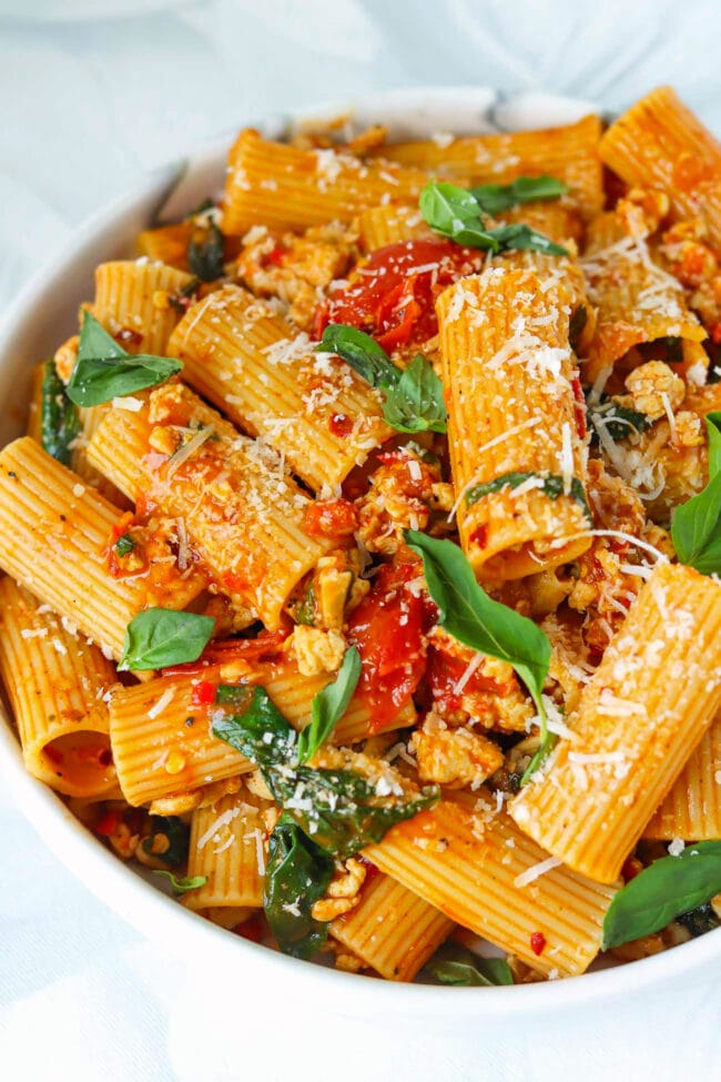 Front view of plate with harissa pasta with cherry tomatoes, spinach, and basil topped with grated parmesan cheese.