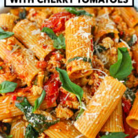 Front view of plate with harissa and cherry tomato rigatoni with spinach and basil topped with grated parmesan. Text overlay "Harissa Pasta with Cherry Tomatoes" and "That Spicy Chick".