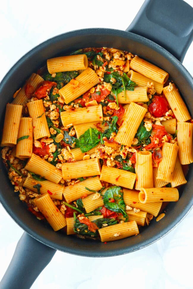 Harissa pasta with cherry tomatoes, ground chicken, spinach and basil in a pan.