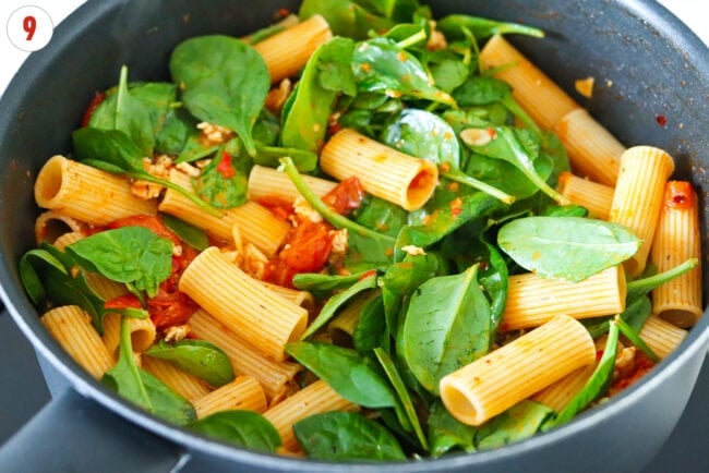 Harissa pasta with burst cherry tomatoes sauce, spinach and ground chicken in a skillet.