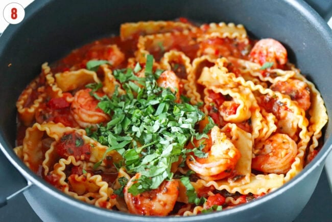 Sliced basil in pan with pasta puttanesca with shrimp.