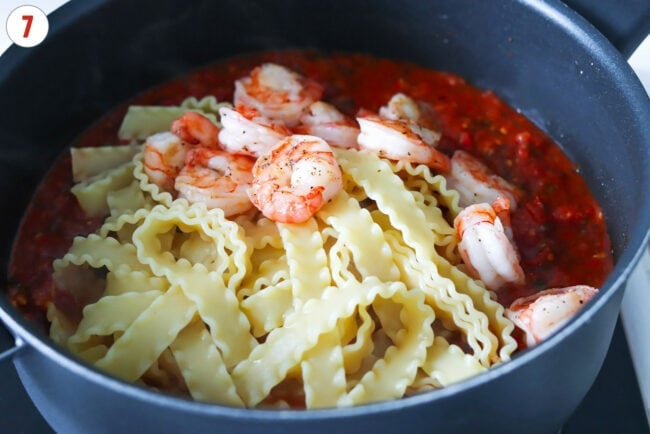 Mafaldine pasta and cooked shrimp in a pan with spicy tomato sauce.